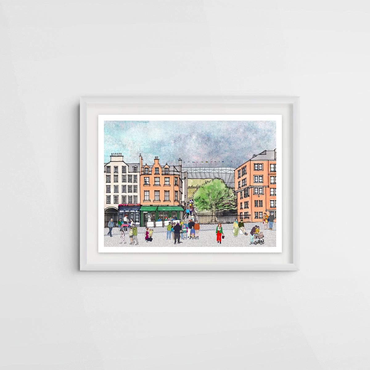 A framed watercolour print of a bustling city square in Edinburgh's Grassmarket, featuring colourful buildings, pedestrians, and a tree, set in a white frame against a light grey wall.