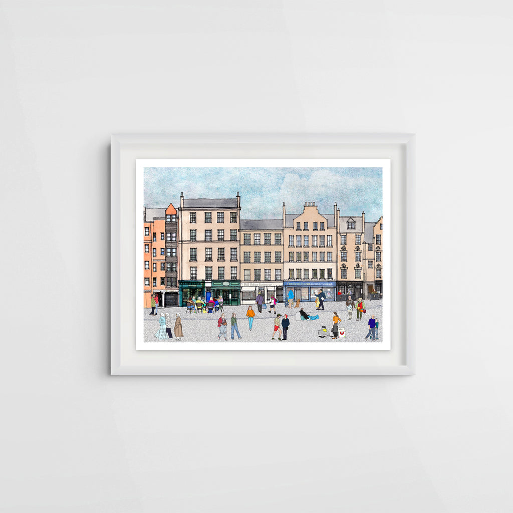 A framed watercolour art print depicting a bustling city square (Edinburgh Grassmarket) with historic buildings and small illustrated figures, displayed on a light grey wall.