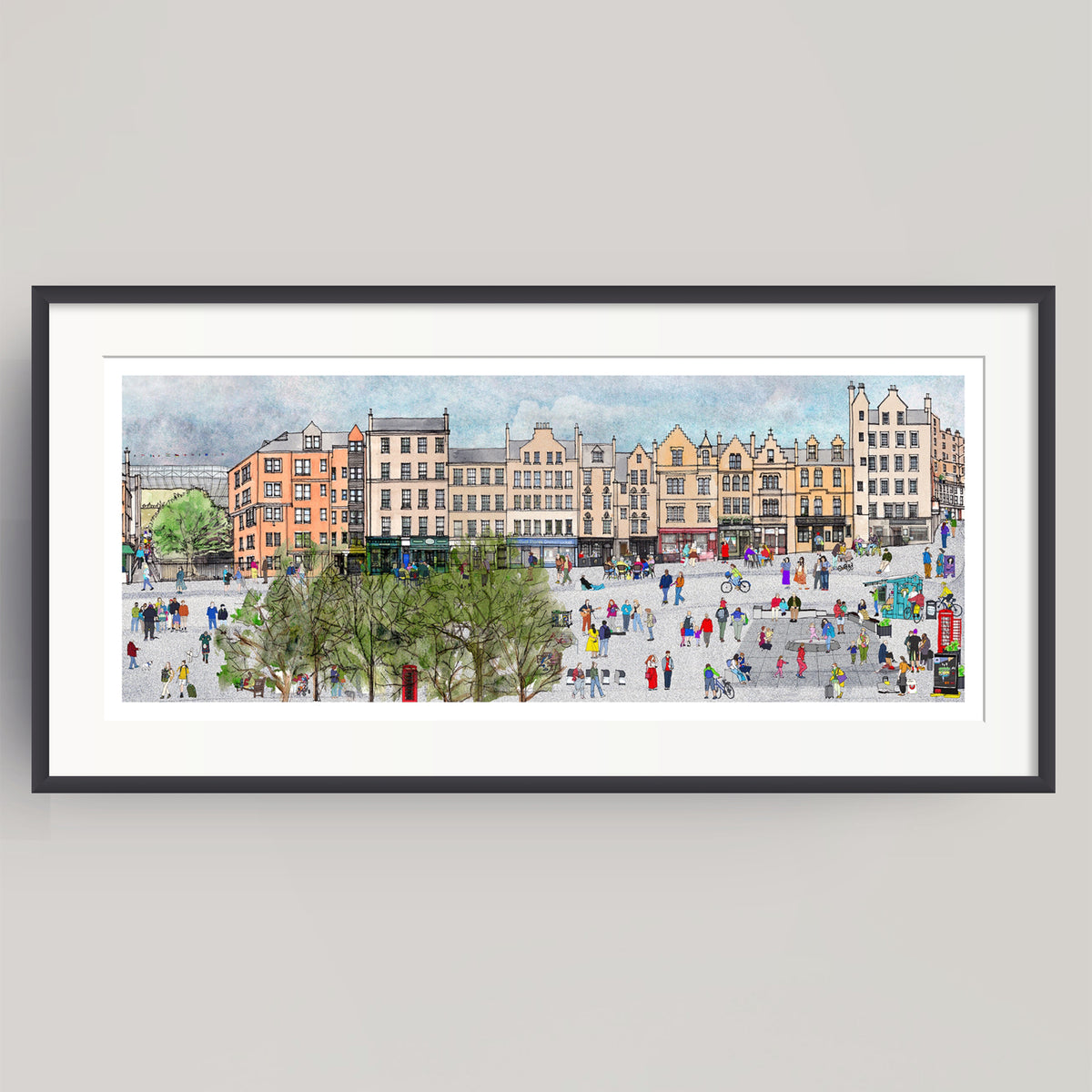 A framed panoramic watercolour print of the bustling city square of Edinburgh's Grassmarket, featuring historic buildings, trees, and numerous small figures of people. The print is presented in a white mat and a sleek black frame against a neutral light gray background.