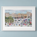 A framed art print depicting a colourful, whimsical scene set during the Edinburgh Festival with people, bicycles, and historic buildings, presented in a white frame against a light blue-grey wall.
