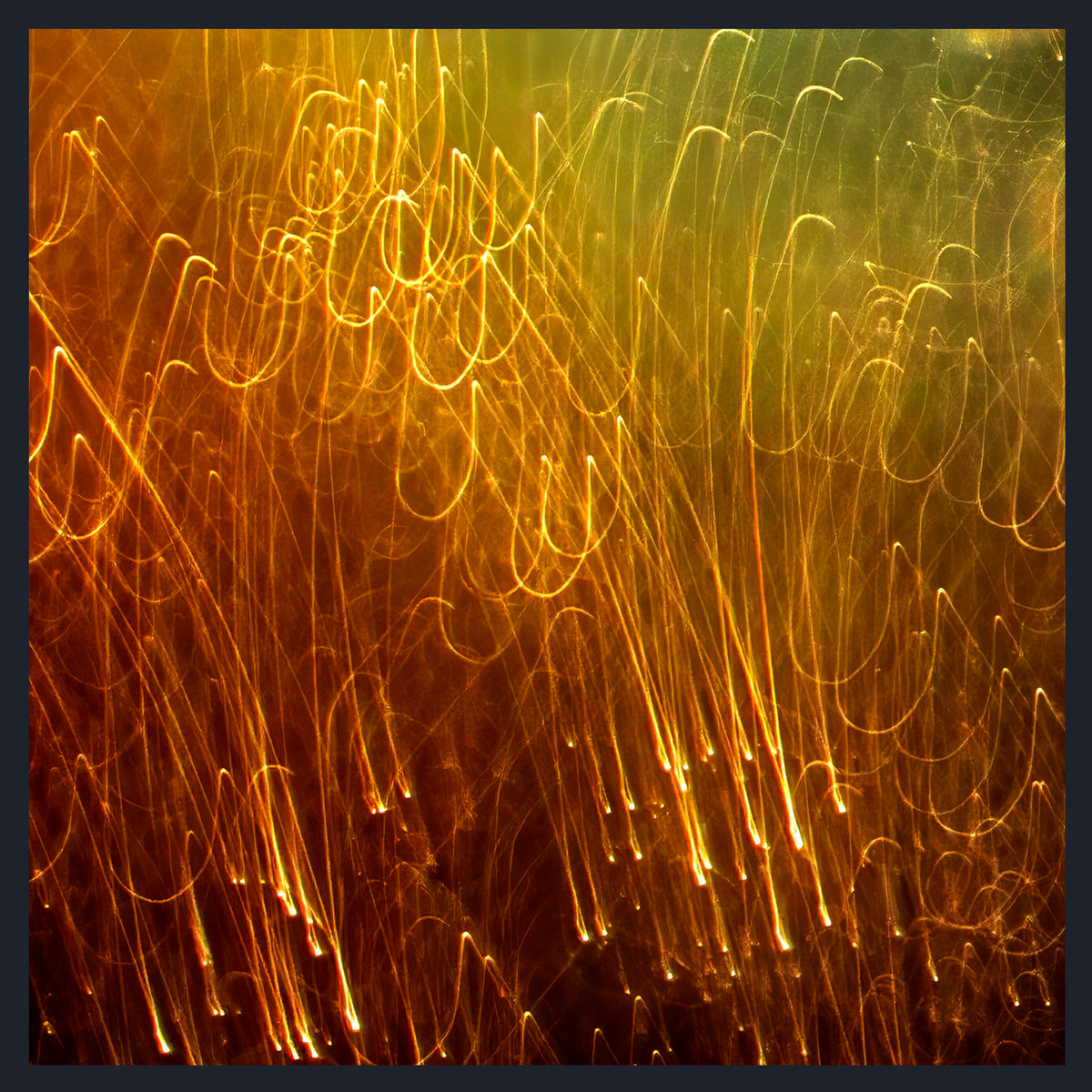 Abstract long-exposure photograph of glowing orange and yellow light trails or sparks against a dark brown and green background, framed by a thin dark border.