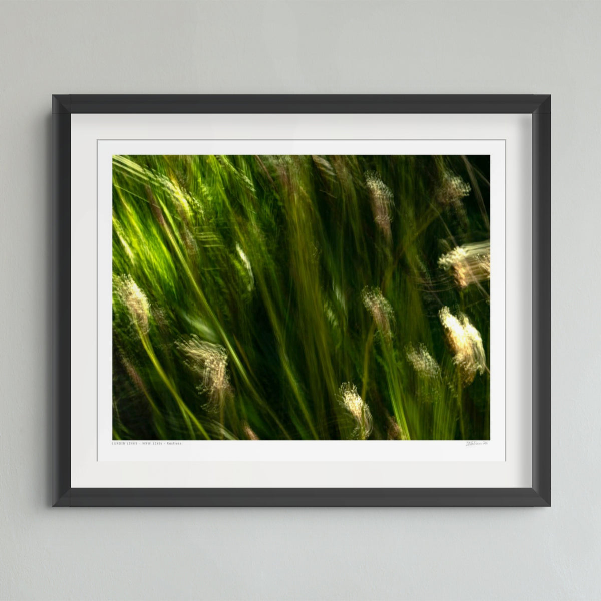 Abstract photographic print featuring blurred vertical streaks of green and yellow-green light with soft glowing beige forms, framed by a dark border.
